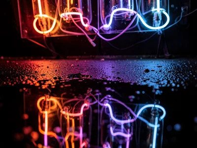 A neon sign reflected in rain on a street: the tubes visible directly above and 