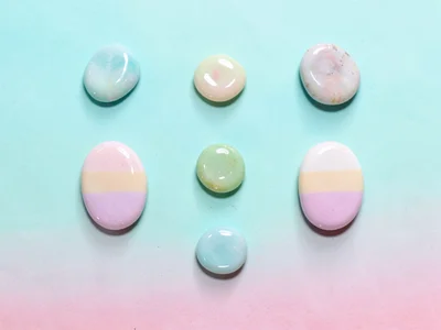 Quietly spaced grid of six glossy stones in graduated pastel tones laid on a sof