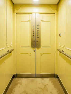 Elevator interior in pale yellow, ornate operator panel, symmetrical buttons, ca