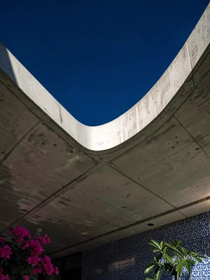 Underside of a cantilevered slab roof — smooth concrete curve against deep blue 