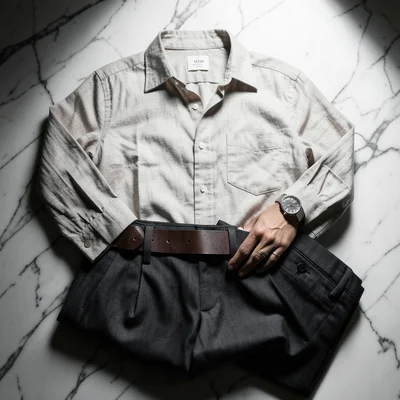 Flat lay of a curated outfit: linen shirt, tailored pants, leather belt, watch, 