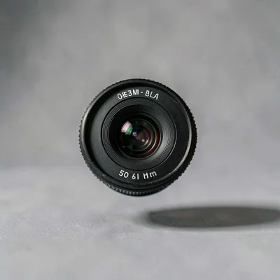Studio composition of a single 50mm prime lens floating mid-frame on a soft grey