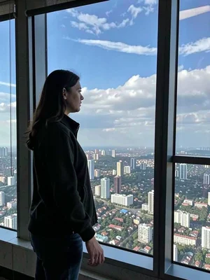 Woman at window of high-rise, city below, clouds level with her, the altitude of