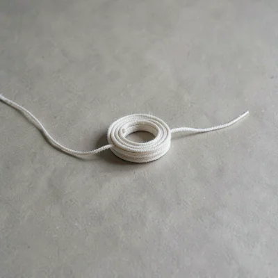 A single coil of pale linen cord resting on warm-grey paper, thread untwisting s