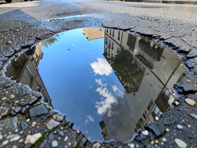 Puddle in cracked asphalt reflecting blue sky, sky visible through broken road s