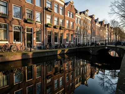 Amsterdam canal houses reflected in still water, bicycles parked on bridge, spri