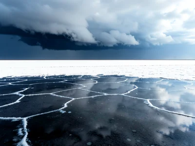 Storm clouds approaching over salt flat — dark cell reflected below, white expan
