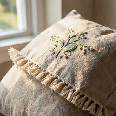 Warm linen close-up of an embroidered pillow with a beaded fringe, gentle window