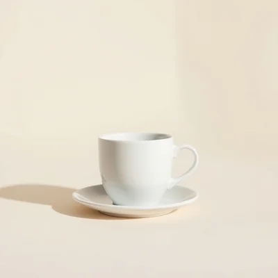 Minimalist studio photograph of a single white ceramic coffee cup on a seamless warm off-white background, clean composi