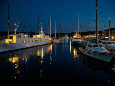 A marina at night: boats lit from within, reflections dancing on dark water, the