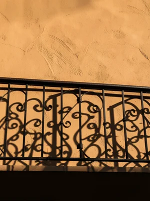 The shadow of a wrought-iron balcony railing cast onto a smooth ochre plaster wa