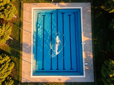 An outdoor swimming pool from directly above, blue rectangle with lane lines, a 