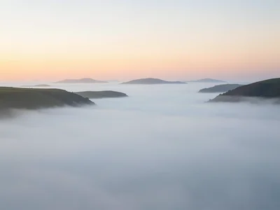 Ground fog rolling across a valley at sunrise, hilltops emerging as islands