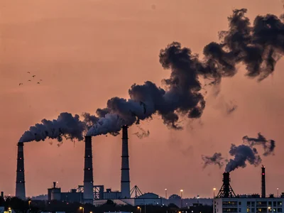 Industrial smokestacks at dusk, structures and smoke plumes black against salmon
