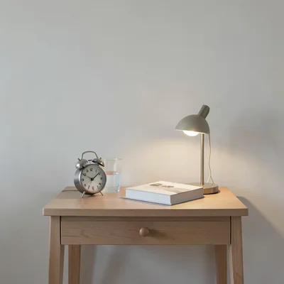 Nightstand with alarm clock, water glass, book, small lamp, simple composition
