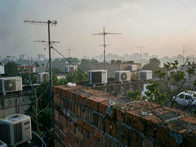 Crumbling brick parapet looks across a rooftop wilderness of AC units and antenn