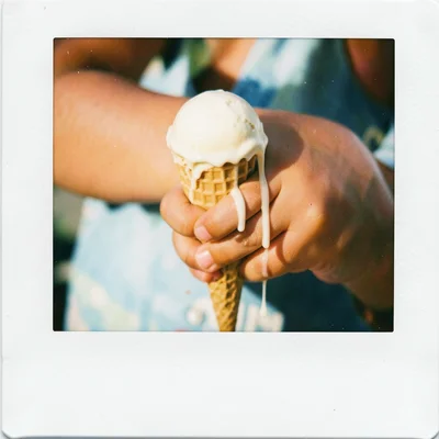 A child's hand holding a melting ice cream cone, drips running down the wrist, s