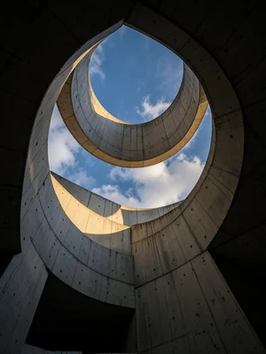 A concrete spiral staircase viewed from below, the helix ascending toward a circ