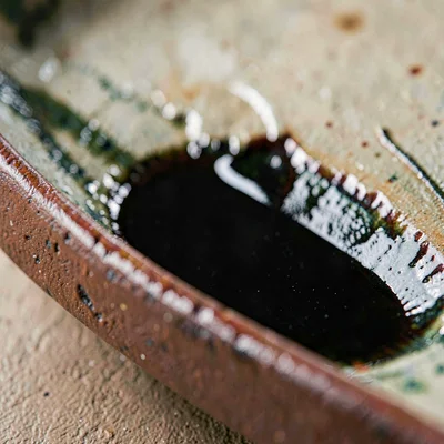 Tenmoku pooling deep black in a hand-formed groove, glaze breaking iron-red at t