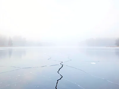 Mirror-still frozen lake stretching into white sky with a hairline crack as the