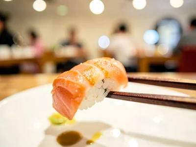Sushi piece on chopsticks, restaurant behind cream