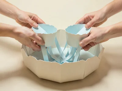 A wide papercraft fountain made of soft-folded paper basins, water suggested by