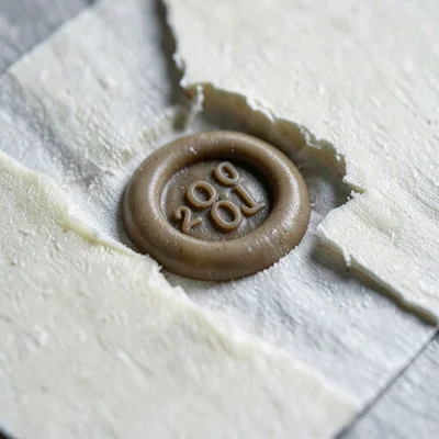 Mineral-cut macro of a wax seal pressed onto ivory paper, cool shadow valleys ar