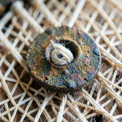 Macro of an oxidized loom heddle with linen thread caught in the eye