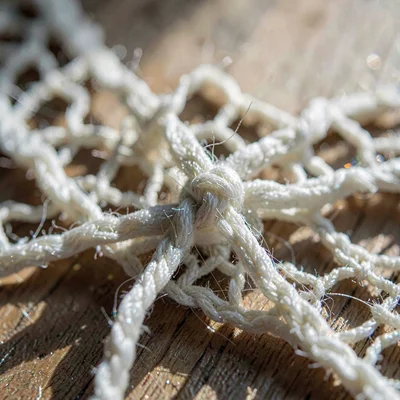 Macro of woven cotton lace knot, fibers crossing under raking light