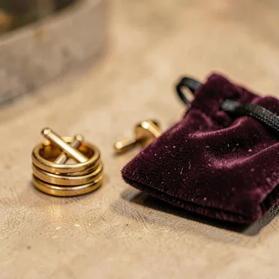 Warm close-up of a stack of folded cufflinks beside a velvet pouch