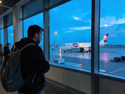 Traveler at terminal window watching plane taxi at blue hour
