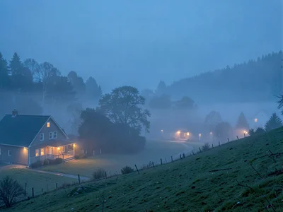 Farmhouse lights glowing through thinning predawn fog