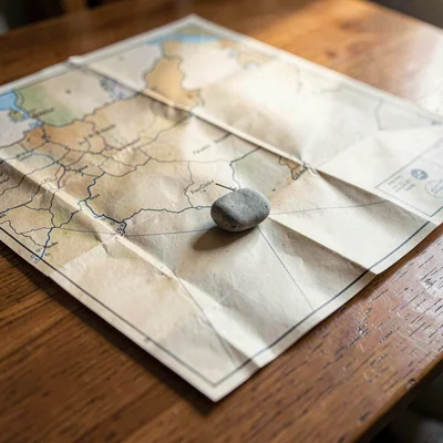 Wide tabletop scene of an unfolded paper map with creases catching light, a smal