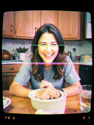 A woman laughing at a kitchen table, her face split by a horizontal band of stat