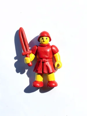 Toy-scale clay knight miniature in primary red and yellow holding a stubby sword