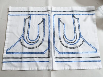 Ritual garment laid flat — full embroidery coverage on front panels, blue accent