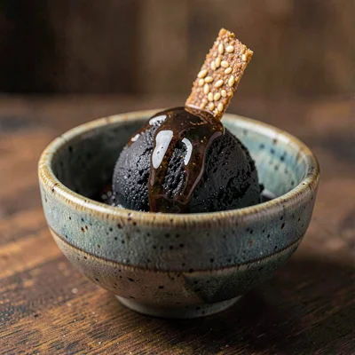 Hand-thrown bowl of black-sesame ice cream with a drizzle of dark honey and a si