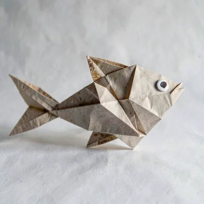 Origami-style paper fish folded from a coffee filter, raking sidelight carving e