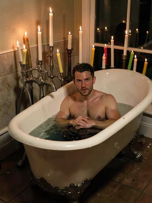 Man submerged in clawfoot bathtub surrounded by thirty mismatched candles