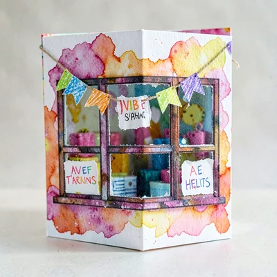 A pop-up paper bookshop window with torn-paper signs and crayon bunting hung acr