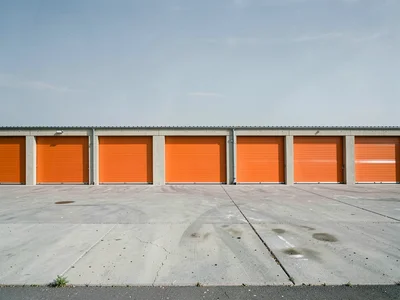 Storage unit facility — repeating orange roll-up doors, concrete drive, flat sky
