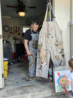 A mechanic's oil-stained coveralls hung beside a child's finger painting in gara