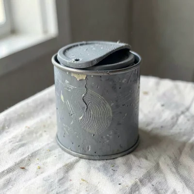 Hammered putty-grey tin can with a slumped lid and fingernail dents along its ri