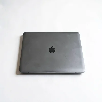 White-on-white still of a single closed laptop centered on a chalk desk, hairlin