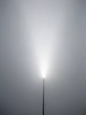Single streetlamp in thick fog, cone of light dissolving into white void