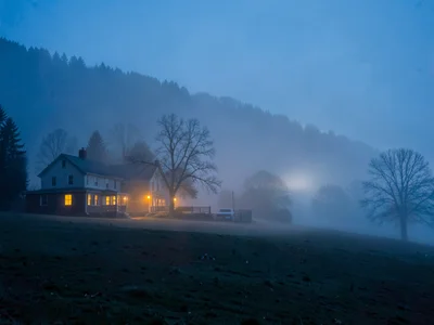 Farmhouse lights glowing through thinning predawn fog
