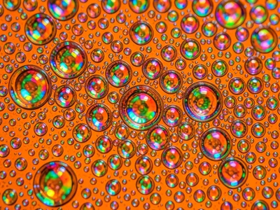 Micro-bubble field on orange-dyed water, hundreds of tiny cells creating uniform