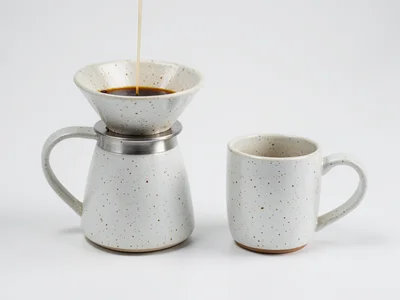 A ceramic pour-over coffee set: dripper on carafe, matching mug, in speckled whi