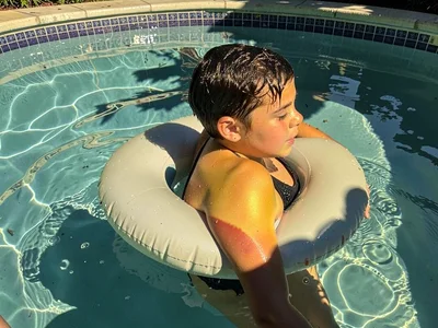Teenager floating on inflatable in above-ground pool, water shadows gone teal, l