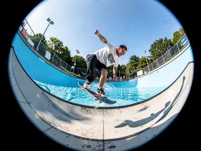 Skater mid-kickflip in empty pool, fisheye bending the coping into a smile, boar